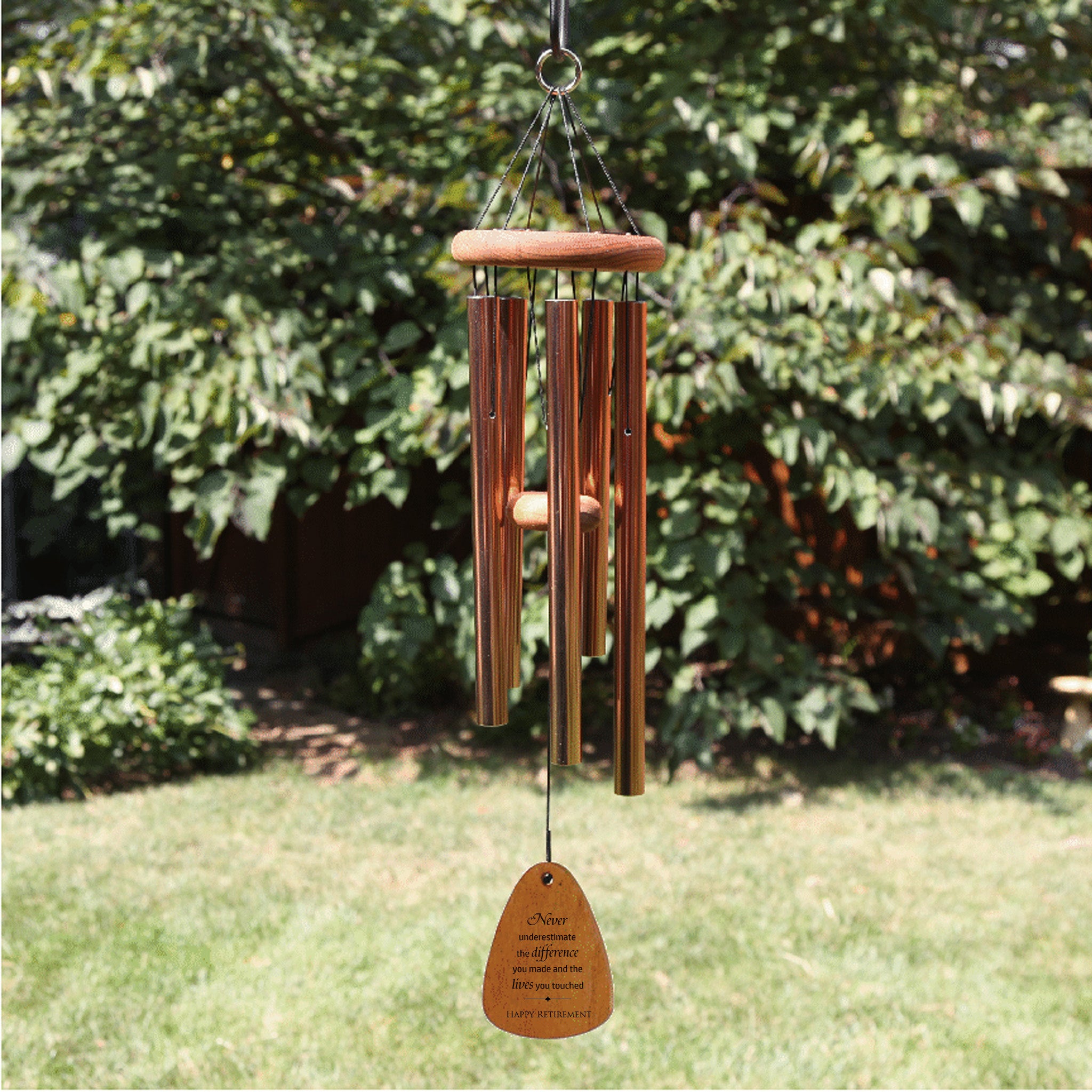 Lifestyle image of bronze wind chime with a wooden wind sail. Shown in a garden setting. 