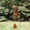 Lifestyle image of bronze wind chime with a wooden wind sail. Shown in a garden setting. 